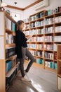 Beautiful girl is studying reading a book while standing on the floor among books in the bookshop