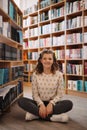 Beautiful girl is studying reading a book while standing on the floor among books in the bookshop