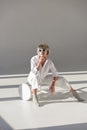 beautiful girl in sunglasses and fashionable white outfit sitting on chair and resting chin on hand Royalty Free Stock Photo