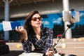 Beautiful girl in sunglasses with map leaning on cabriolet car while dreamily taking photos on cellphone with passport Royalty Free Stock Photo