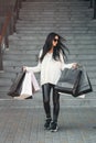 Beautiful girl in sunglasses with paper bags walking out of shopping mall