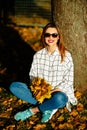 Girl in sunglasses sits under the tree with a bunch of autumn leaves Royalty Free Stock Photo