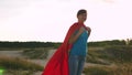 Beautiful girl superhero standing on the field in a red cloak, cloak fluttering in the wind. Slow motion. A young girl