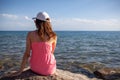 A beautiful girl with long hair and a white cap looks at the blue sea Royalty Free Stock Photo