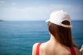 A beautiful girl with long hair and a white cap looks at the blue sea Royalty Free Stock Photo