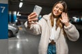 Beautiful girl takes selfie in the underground parking. Fashionable young woman with smartphone talking on video call Royalty Free Stock Photo