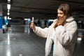 Beautiful girl takes selfie in the underground parking. Fasionable young woman with smartphone. Royalty Free Stock Photo