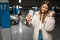 Beautiful girl takes selfie in the underground parking. Fasionable young woman with smartphone. Royalty Free Stock Photo