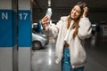 Beautiful girl takes selfie in the underground parking. Fasionable young woman with smartphone. Royalty Free Stock Photo