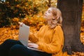 A beautiful girl sits in an autumn park with a laptop. The student studies on the street. The girl closed her eyes and Royalty Free Stock Photo