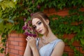 Beautiful girl in tender prom dress on brick wall and green ivy bush with flowers background. Female portrait Royalty Free Stock Photo