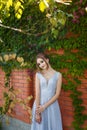 Beautiful girl in tender prom dress on brick wall and green ivy bush with flowers background. Female portrait on spring Royalty Free Stock Photo