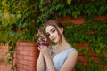 Beautiful girl in tender prom dress on brick wall and green ivy bush with flowers background. Female portrait on spring landscape. Royalty Free Stock Photo