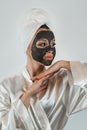 beautiful girl in towel applying black caly mask on face on white gray