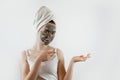 beautiful girl in towel applying black caly mask on face on white gray