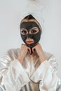 beautiful girl in towel applying black caly mask on face on white gray