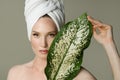 A beautiful girl with towel on her head holds a green leaf in her hands. Cleanliness and care