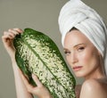 A beautiful girl with towel on her head holds a green leaf in her hands. Cleanliness and care