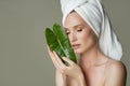 A beautiful girl with towel on her head holds a green leaf in her hands. Cleanliness and care