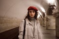 Beautiful girl in trench coat and red beret intently looking in camera waiting train at subway station Royalty Free Stock Photo