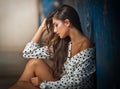 Beautiful girl with unbuttoned shirt posing, old wall with peeling blue paint on background. Pretty brunette sitting on the floor. Royalty Free Stock Photo