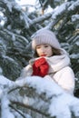Beautiful girl in a warm hat and mittens stands among the snow-covered pine trees. Sunny winter day Royalty Free Stock Photo
