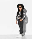Stylish asian girl in jeans and a fashionable plaid shirt and wide-brimmed hat, sunglasses, posing on a light studio background Royalty Free Stock Photo