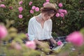 Beautiful girl wearing hat with book sitting on grass in rose gaden Royalty Free Stock Photo