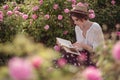 Beautiful girl wearing hat with book sitting on grass in rose gaden Royalty Free Stock Photo