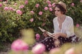 Beautiful girl wearing hat with book sitting on grass in rose gaden Royalty Free Stock Photo