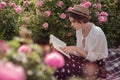 Beautiful girl wearing hat with book sitting on grass in rose gaden Royalty Free Stock Photo