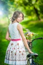 Beautiful girl wearing a nice white dress having fun in park with bicycle. Healthy outdoor lifestyle concept. Vintage scenery Royalty Free Stock Photo