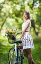 Beautiful girl wearing a nice white dress having fun in park with bicycle. Healthy outdoor lifestyle concept. Vintage scenery