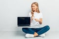 Beautiful girl wearing white t-shirt showing blank laptop screen sitting on floor on grey background Royalty Free Stock Photo