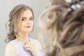 Beautiful girl with a wedding hairstyle looks at herself in the mirror, portrait of a young girl. beautiful make-up. Royalty Free Stock Photo