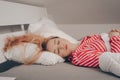 A beautiful girl on a white bed in red striped pajamas is sleeping. Healthy sleep. Woman with closed eyes and long sutra hair on Royalty Free Stock Photo