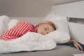 A beautiful girl on a white bed in red striped pajamas is sleeping. Healthy sleep. Woman with closed eyes and long sutra hair on Royalty Free Stock Photo