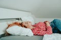 A beautiful girl on a white bed in red striped pajamas is sleeping. Healthy sleep. Woman with closed eyes and long sutra hair on Royalty Free Stock Photo