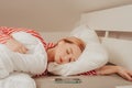 A beautiful girl on a white bed in red striped pajamas is sleeping. Healthy sleep. Woman with closed eyes and long sutra hair on Royalty Free Stock Photo