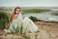 Beautiful girl in a white dress sits on the seashore under the gusts of a cold wind.