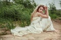 Beautiful girl in a white dress is sitting on the beach and looking back. Royalty Free Stock Photo