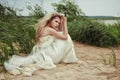 Beautiful girl in a white dress is sitting on the beach and looking into the distance. Royalty Free Stock Photo