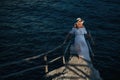 A beautiful girl in a white dress stands on the pier near the sea.Woman in Greece near the sea at sunset