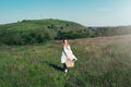 Beautiful girl in white dress with straw bag and wildflowers runs in meadow