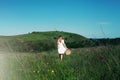 Beautiful girl in white dress with straw bag and wildflowers runs in meadow