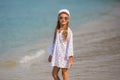 Beautiful girl in a white dress and sunglasses walking on the beach, blue sea in background Royalty Free Stock Photo