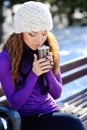 Beautiful girl in white hat sitting on a bench with a cup of coffee in the winter Royalty Free Stock Photo