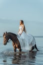 Beautiful girl in a white long dress riding a horse. Bride in the lake on horseback. Royalty Free Stock Photo