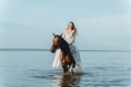 Beautiful girl in a white long dress riding a horse. Bride in the lake on horseback. Royalty Free Stock Photo