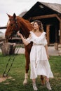 Beautiful girl in a white sundress next to a horse on an old ranch Royalty Free Stock Photo